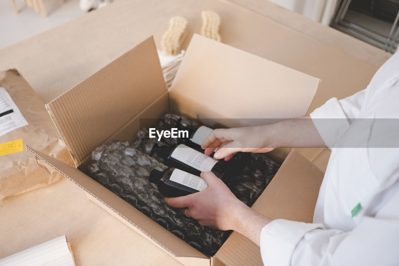 High angle view of female owner unpacking cardboard box containing bottles in workshop