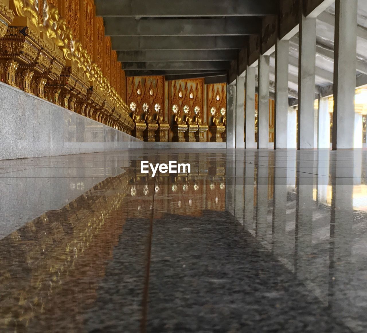 Golden buddha statues reflection on marble flooring at temple