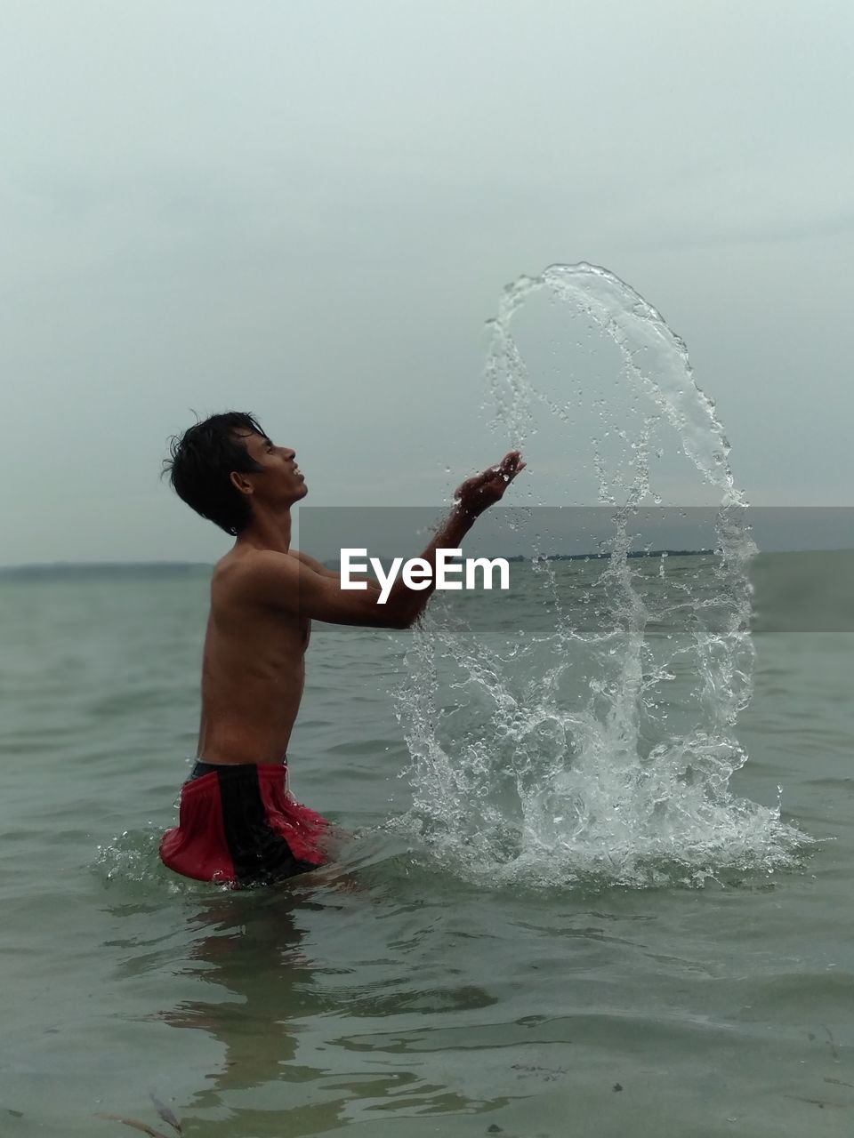 Shirtless man splashing water in sea against sky