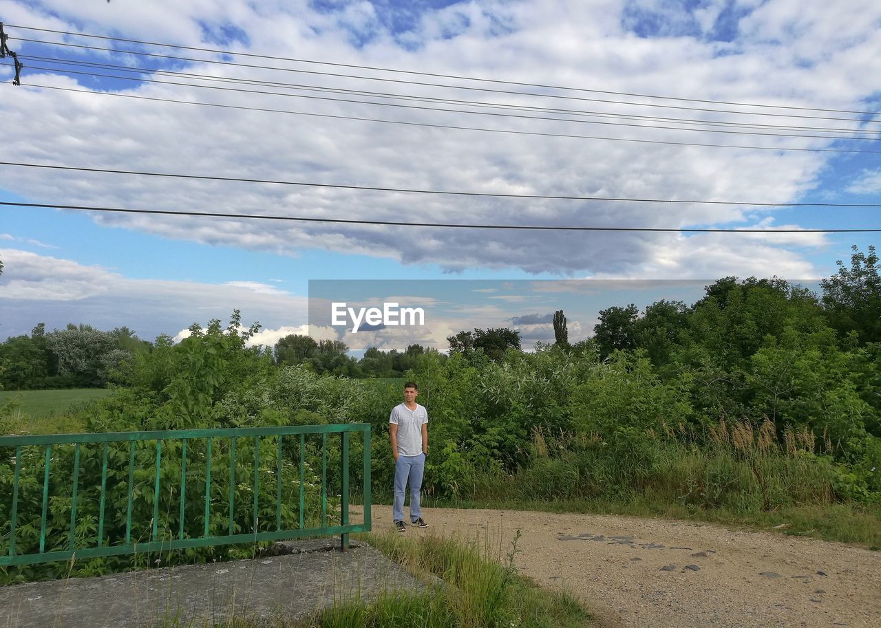 Man standing on footpath against cloudy sky