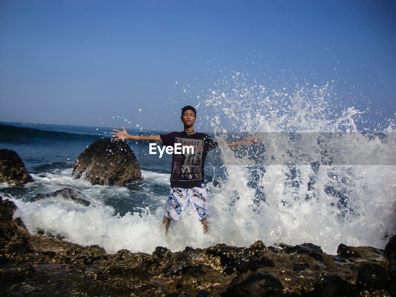 Waves splashing on man standing at beach against sky