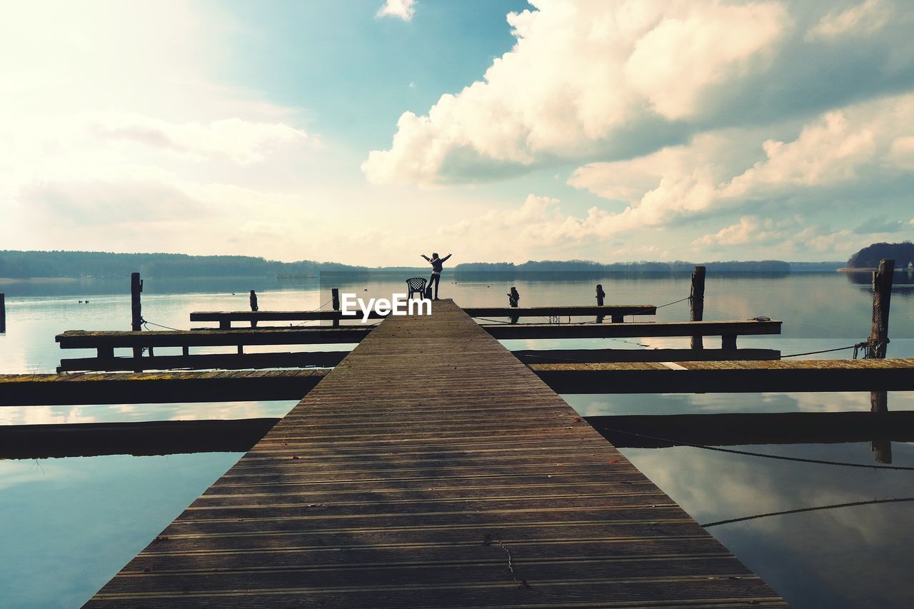 View of person on jetty in sea against cloudy sky