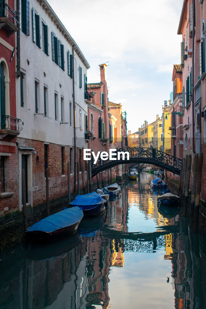 Boats moored in canal by buildings against sky in city