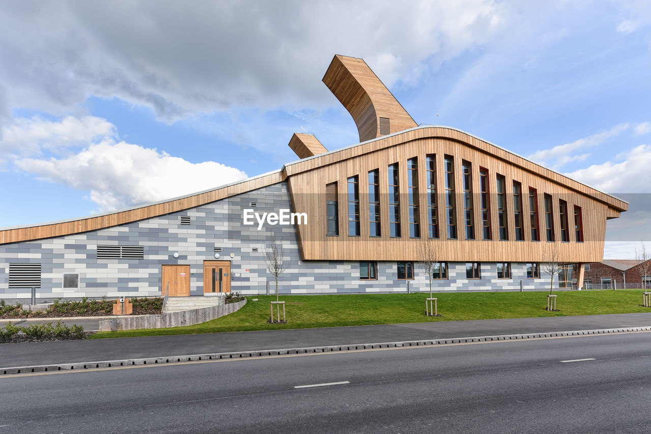 Modern building by road against cloudy sky