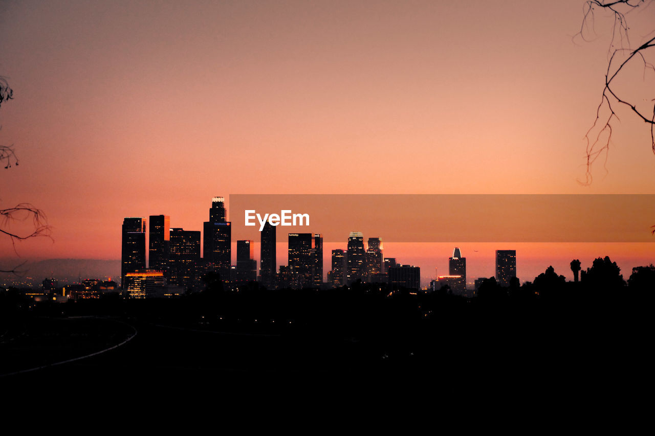 Silhouette buildings against orange sky during sunset