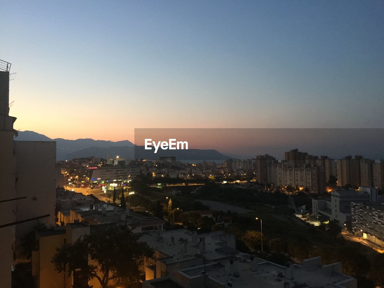 HIGH ANGLE VIEW OF ILLUMINATED CITY BUILDINGS AGAINST CLEAR SKY