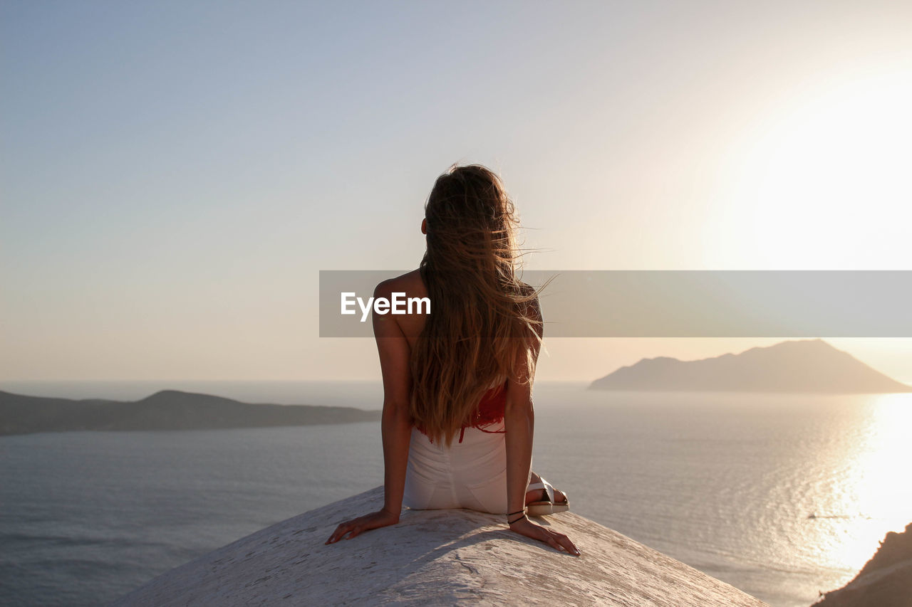 Girl dressed in white and red sitting on the roof of white church overlooking the mediterranean sea