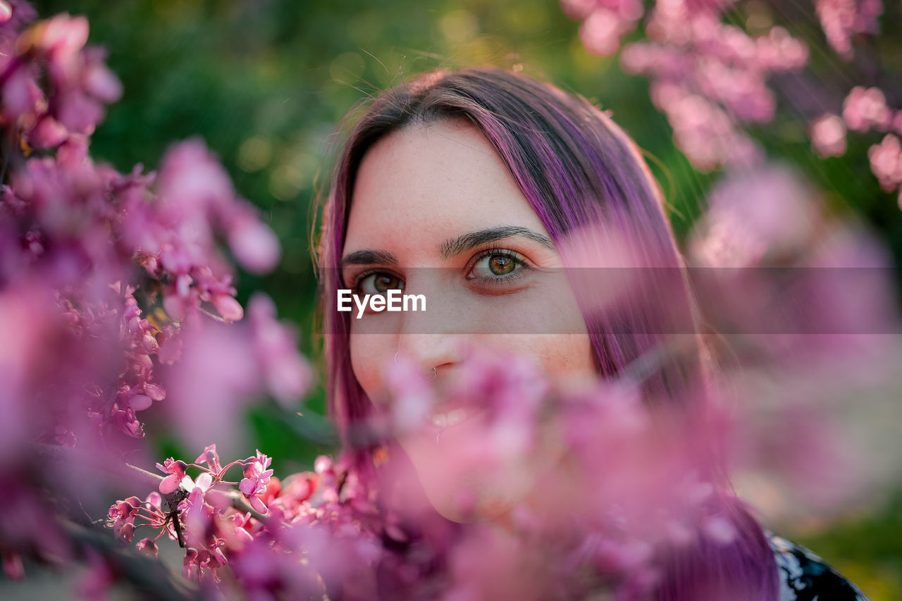 Closeup crop female with green eyes standing near blossoming tree in lush garden