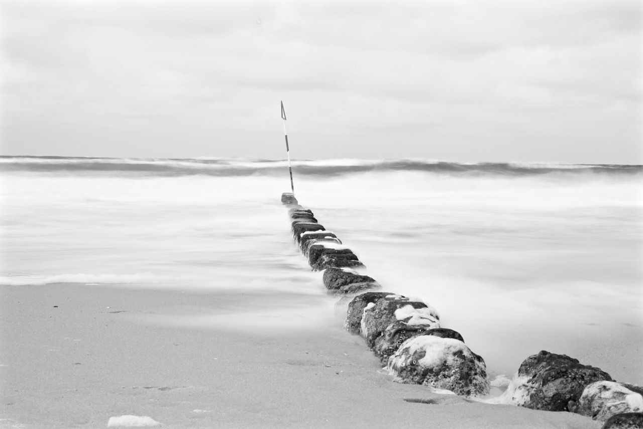 Metal post on rock in sea against sky