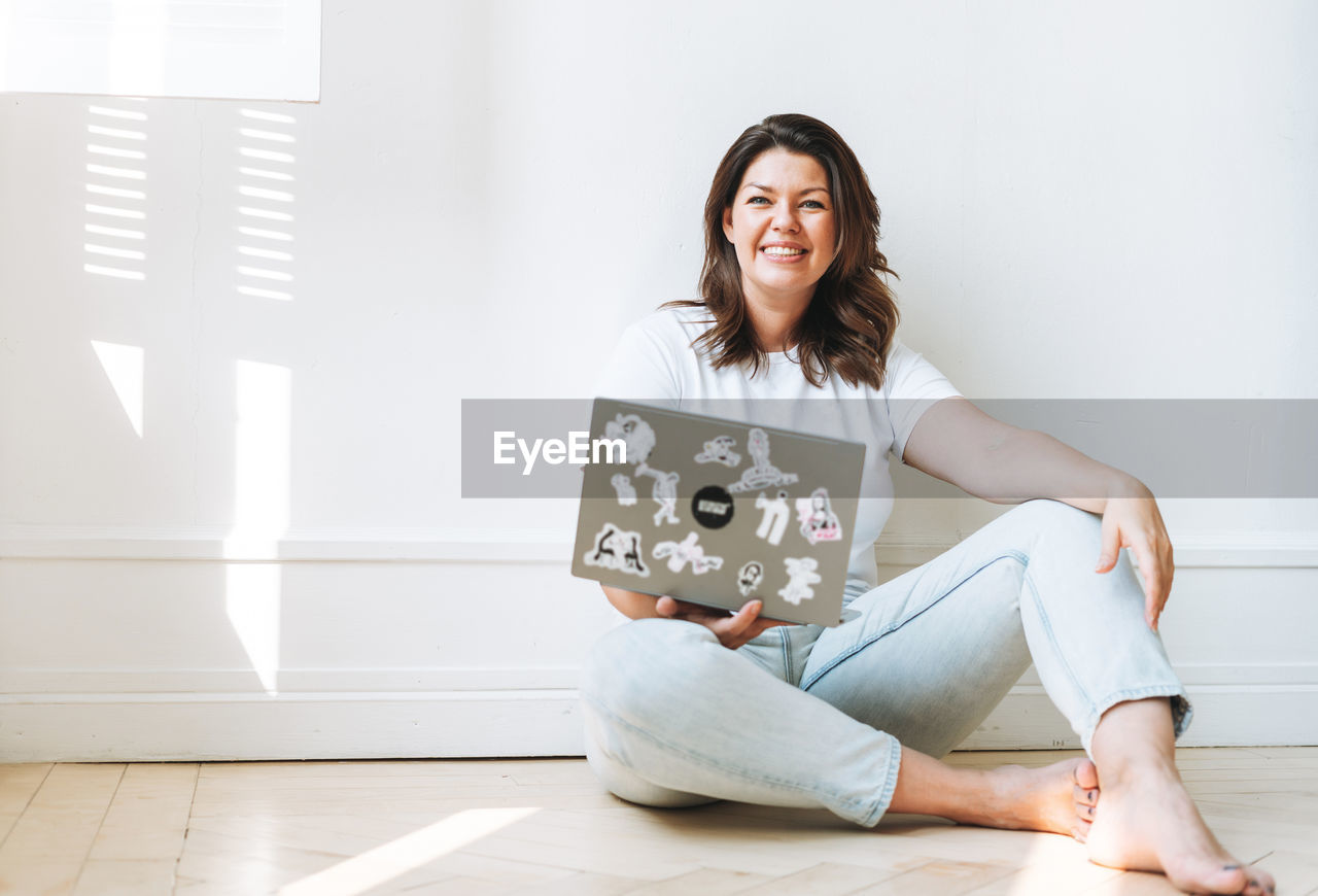 PORTRAIT OF A SMILING YOUNG WOMAN SITTING ON FLOOR