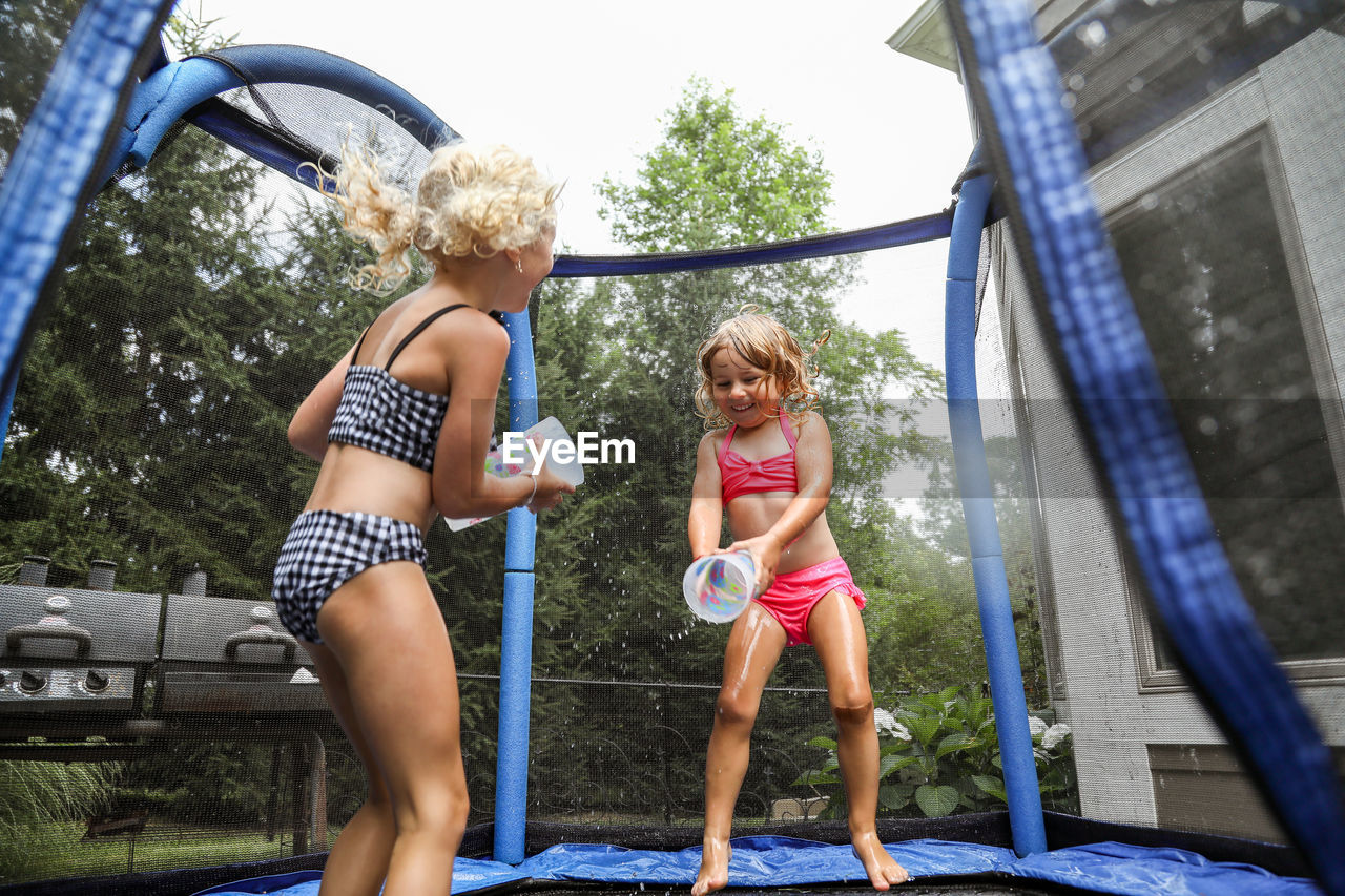 Sisters laughing having water fight on trampoline in summer