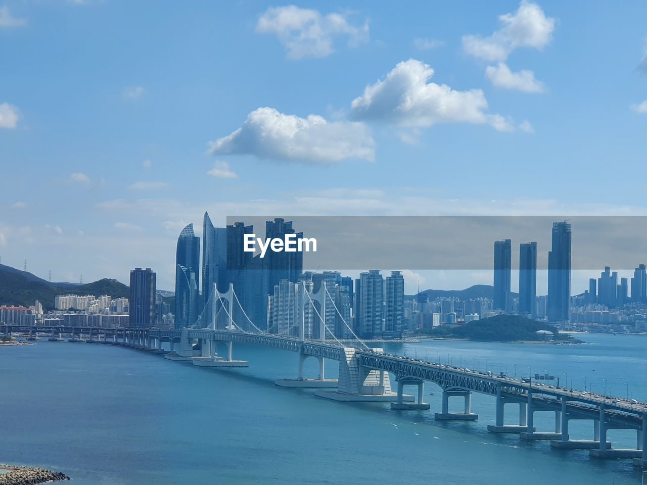 Bridge over river by city buildings against sky