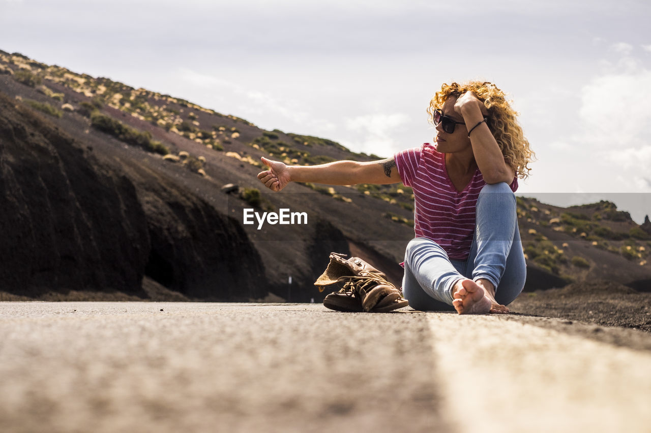 Woman hitchhiking while sitting on road