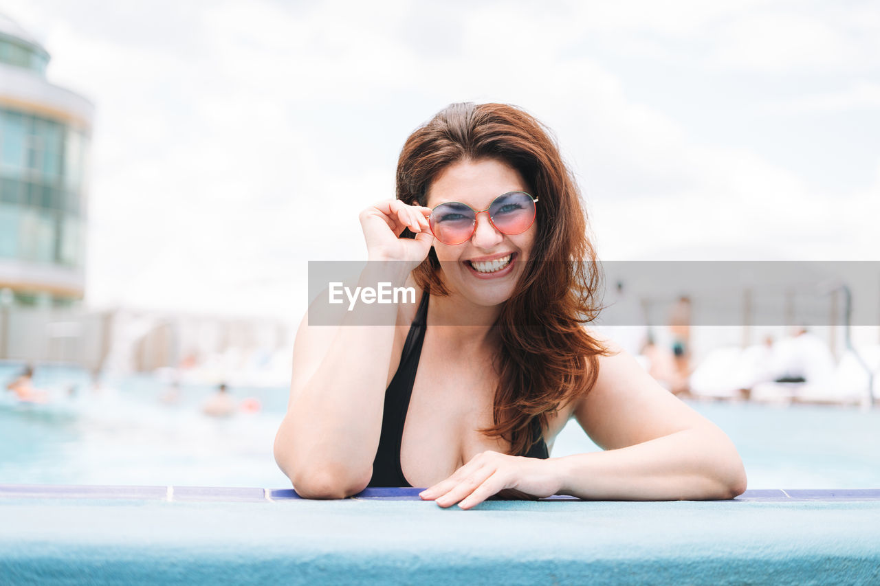 Stylish happy young woman plus size body positive in black swimsuit and sunglasses in pool