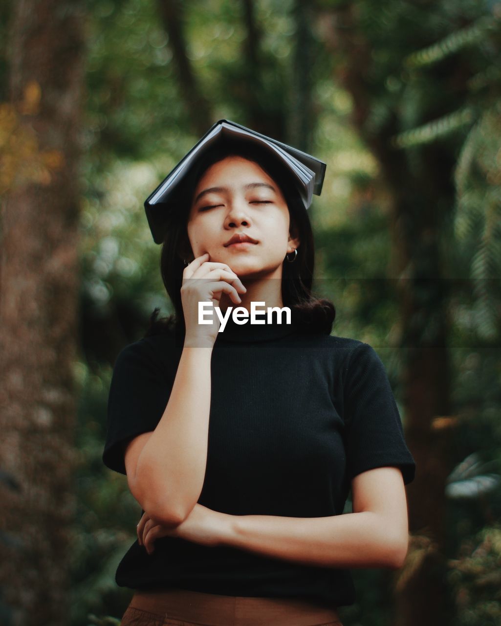 YOUNG WOMAN WEARING HAT STANDING AGAINST TREES