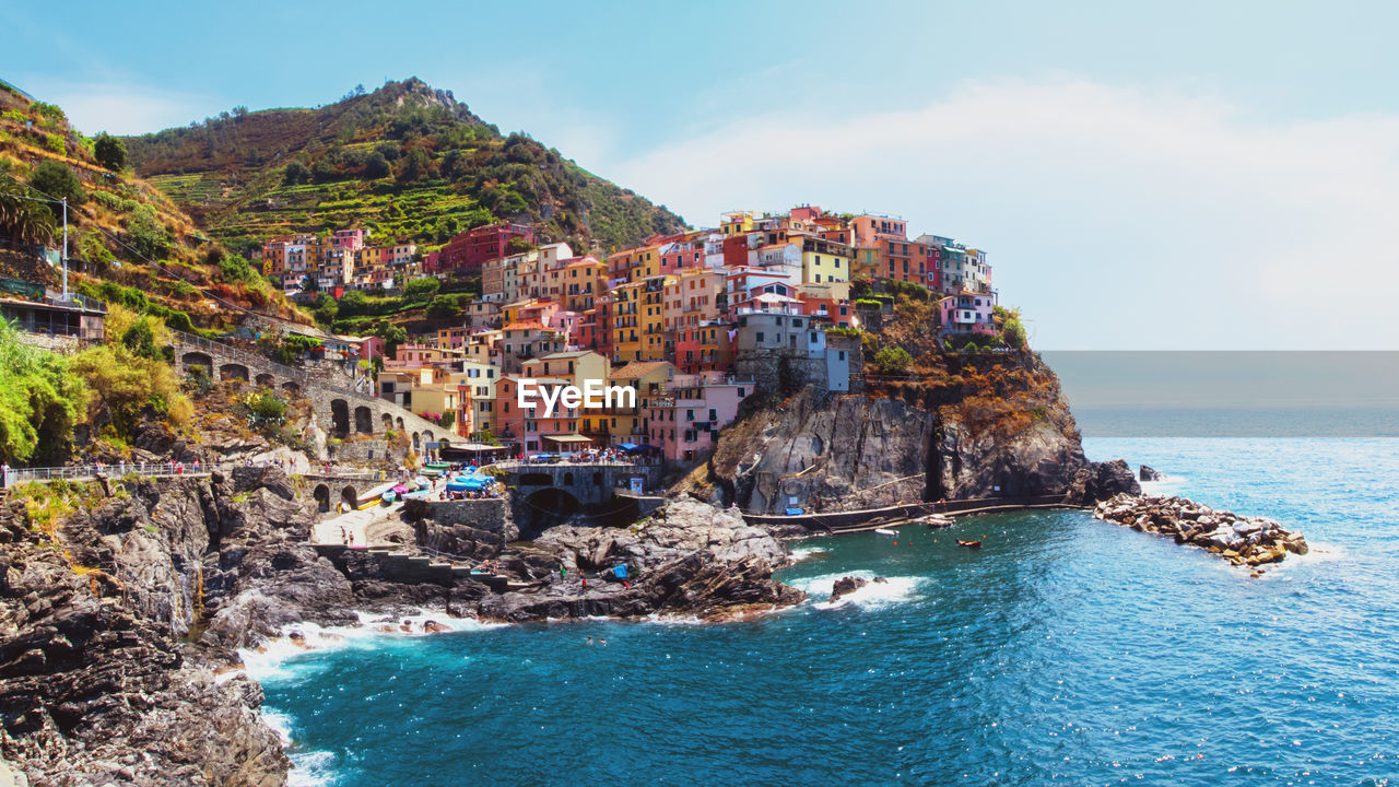 Sea by buildings on cliff against sky