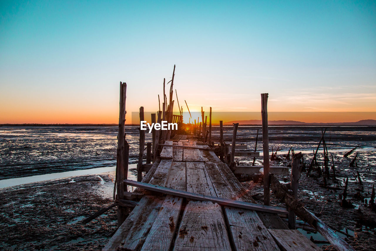 WOODEN POSTS ON BEACH DURING SUNSET