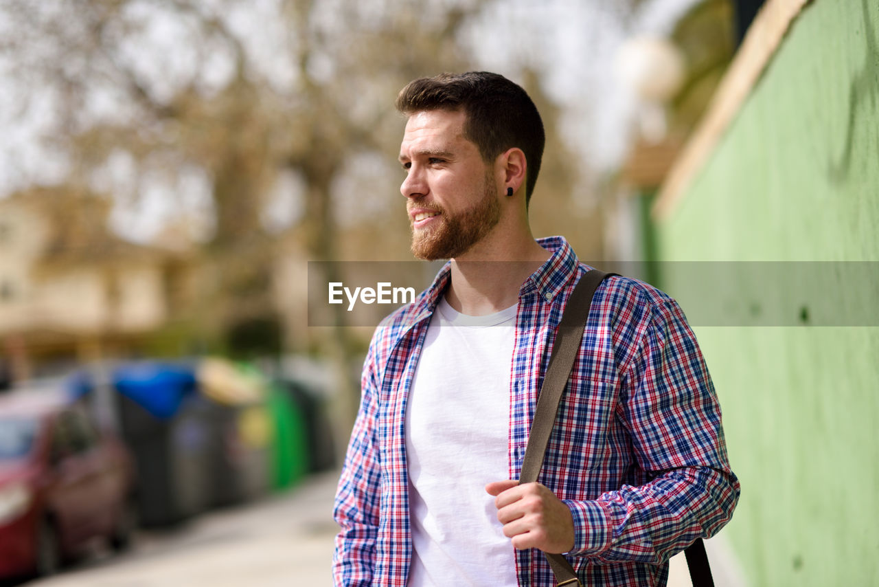 Young man with side bag looking away outdoors