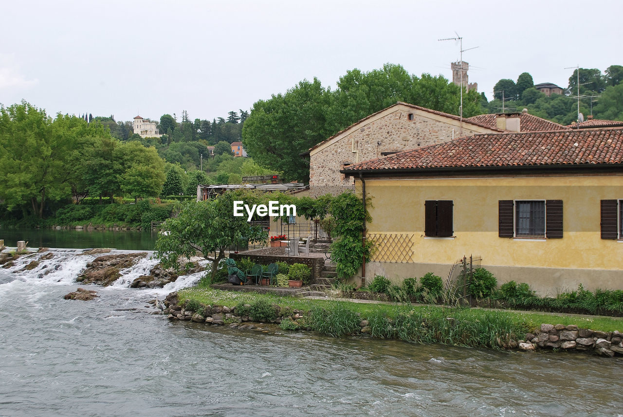 TREES AND HOUSES BY RIVER AGAINST BUILDING