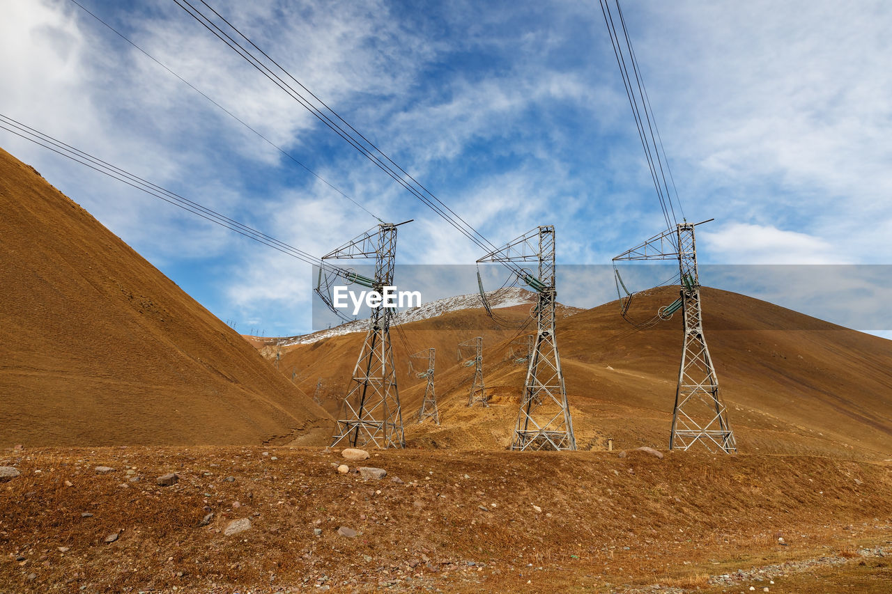 ELECTRICITY PYLON ON FIELD BY MOUNTAIN AGAINST SKY