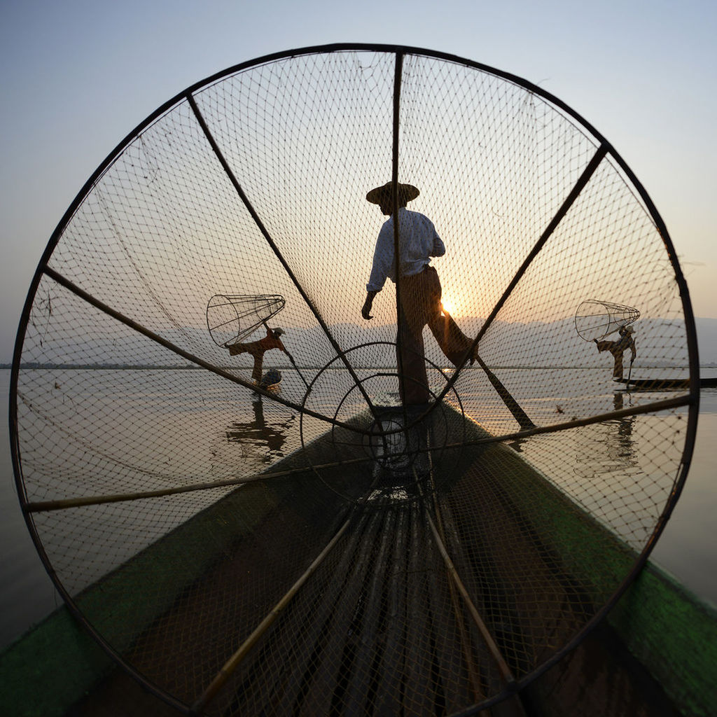 Men fishing in lake during sunset