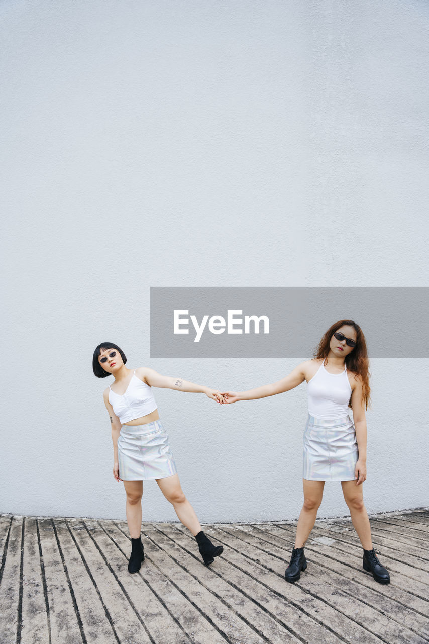 Full length of lesbian couple holding hands standing against wall outdoors