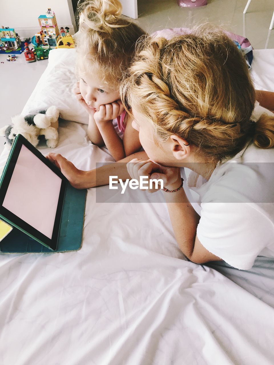 High angle view of mother with daughter using digital tablet while lying on bed at home