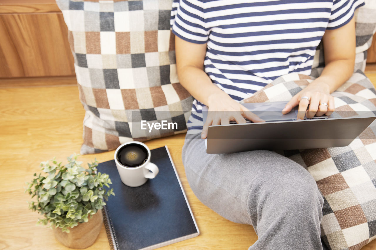 Lay flat view of asian woman working at home with laptop and black coffee on wooden floor 
