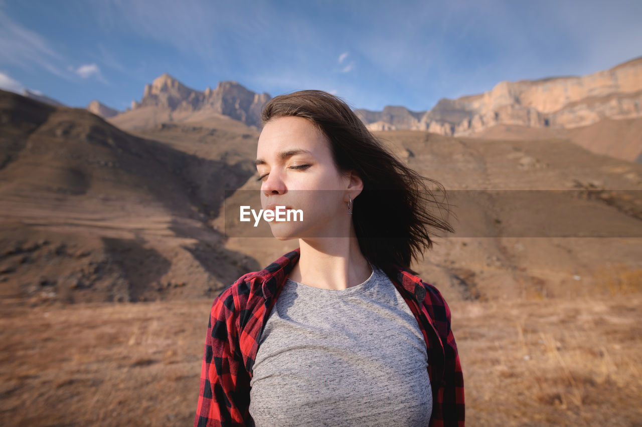 Young attractive woman stands in a shirt against a background of mountains