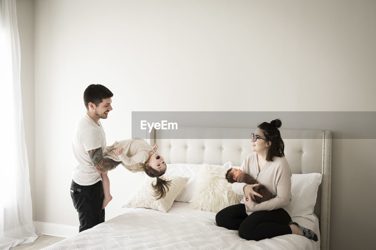 Happy millennial family plays together on white bed at home