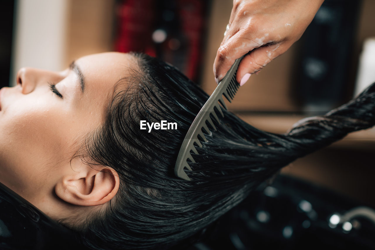 Cropped hand of hairdresser combing woman hair in salon