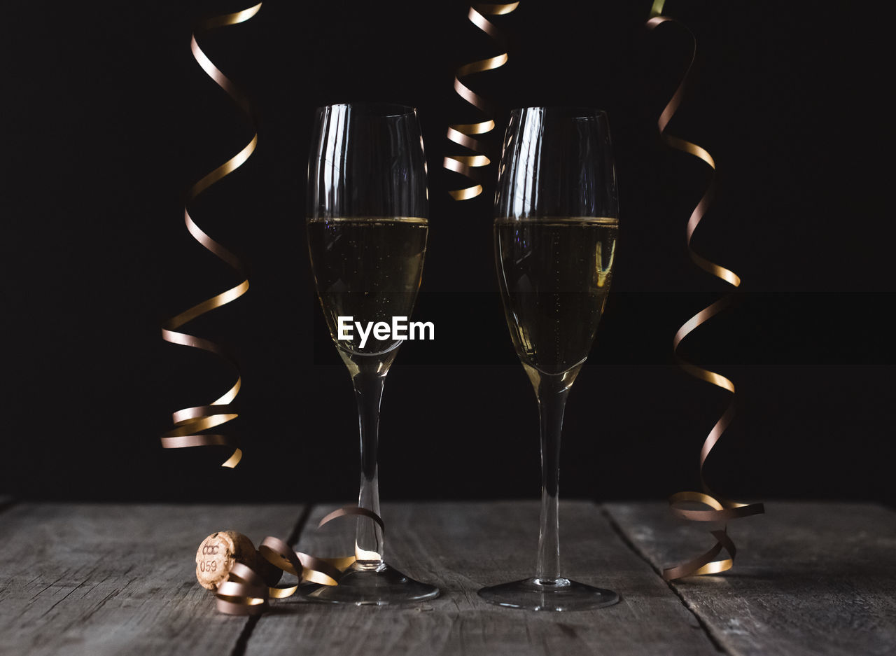 Two glasses of champagne on wooden table with black background.