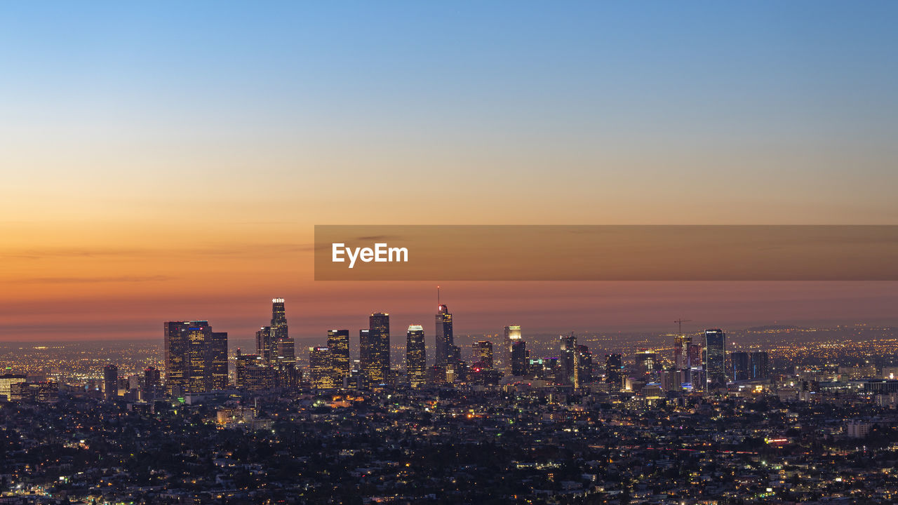 Illuminated cityscape against sky during sunset