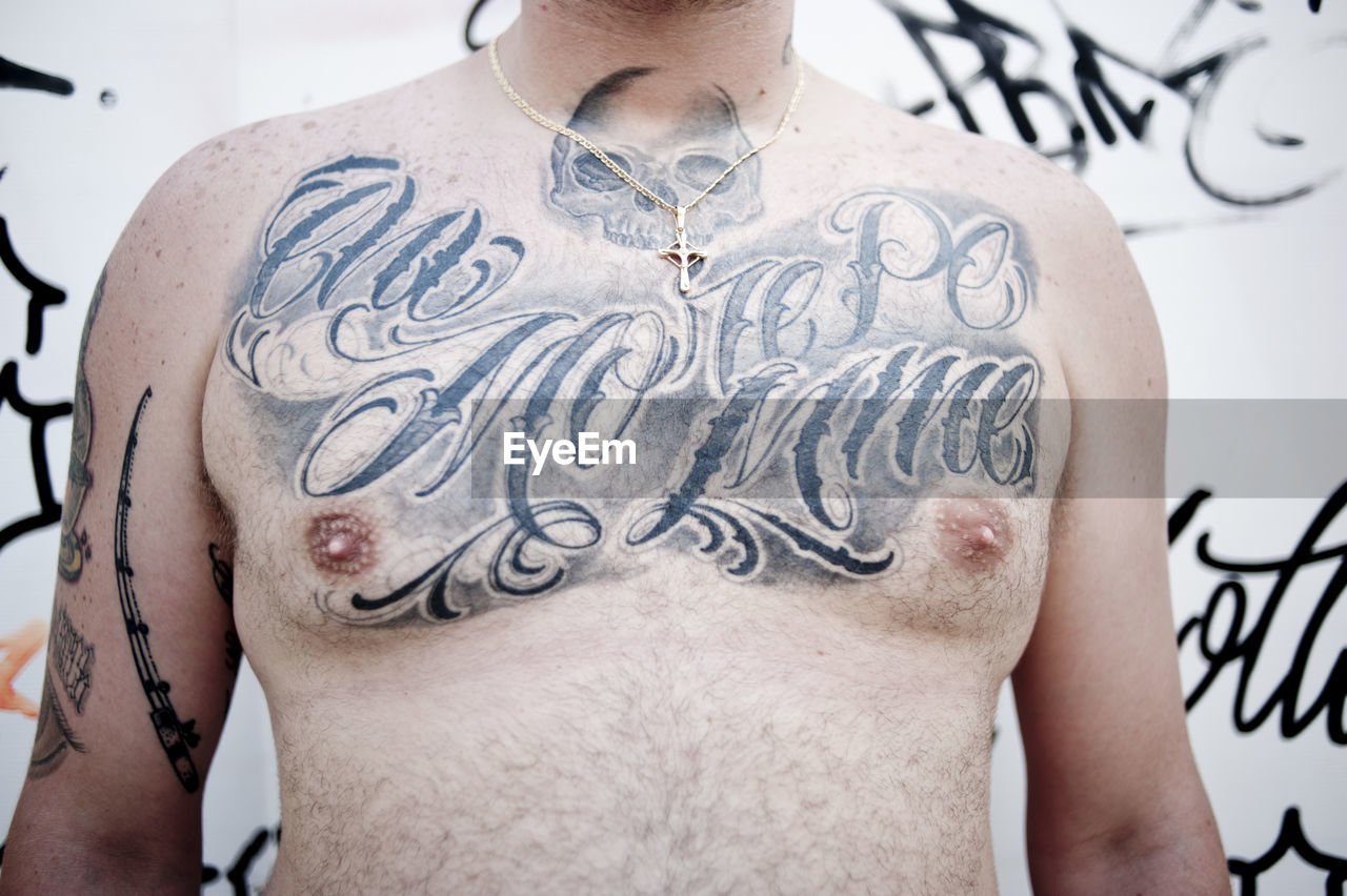 Midsection of man with tattoo against wall