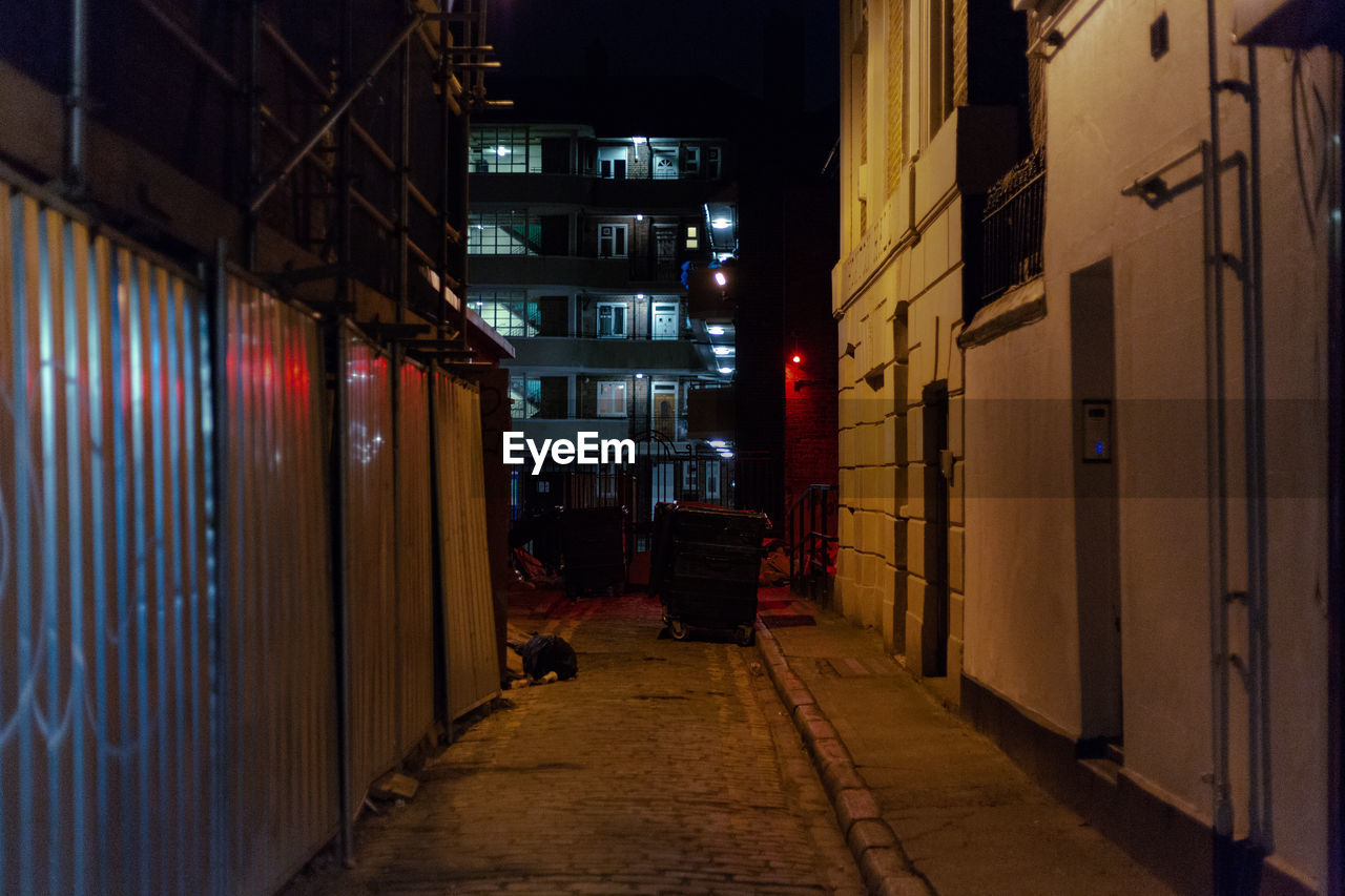 NARROW ALLEY AMIDST BUILDINGS IN CITY AT NIGHT