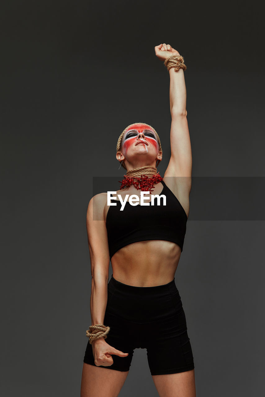 portrait of young woman with arms raised standing against black background