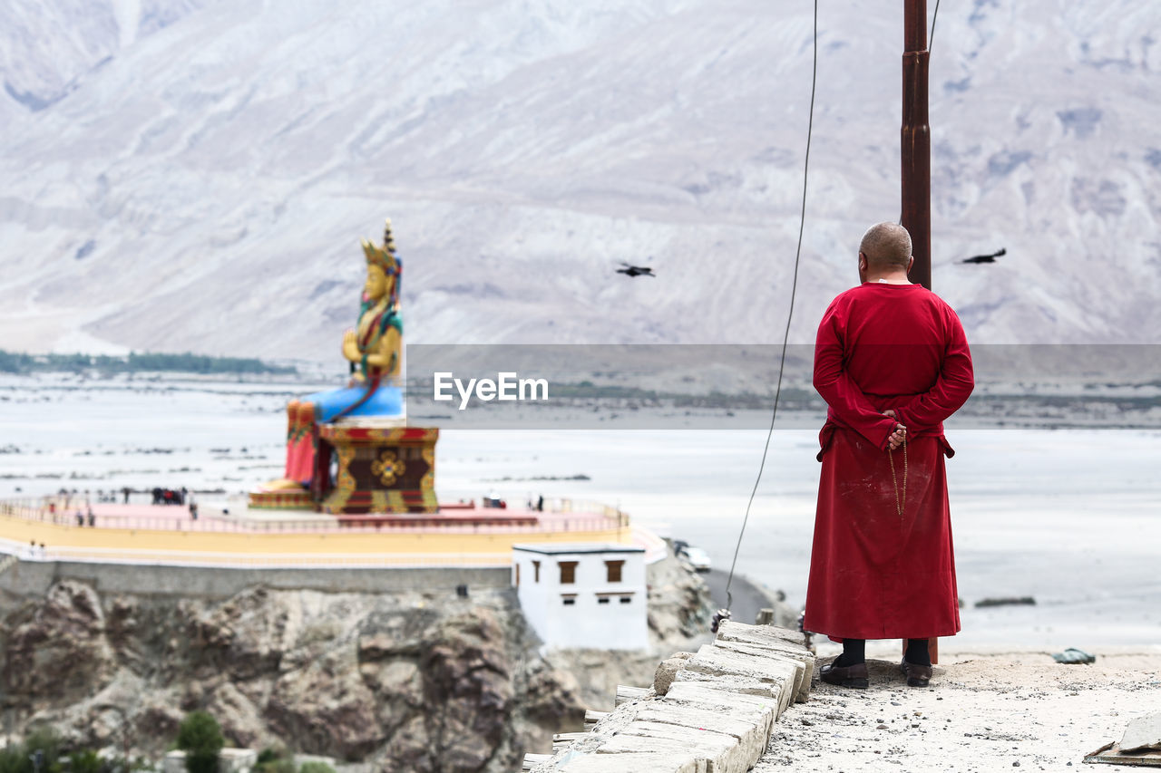 Rear view of monk standing at temple against mountains