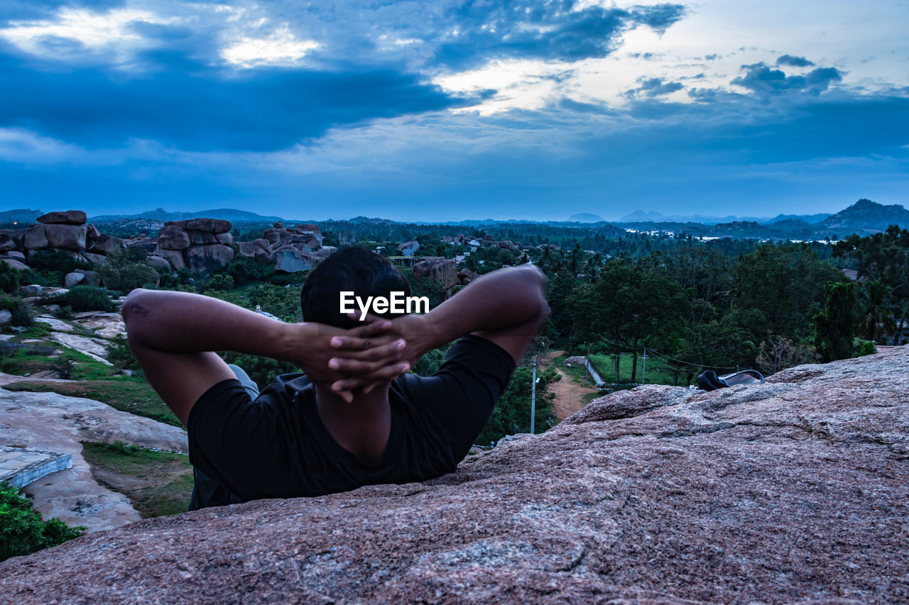 Rear view of man sitting on rock looking at view