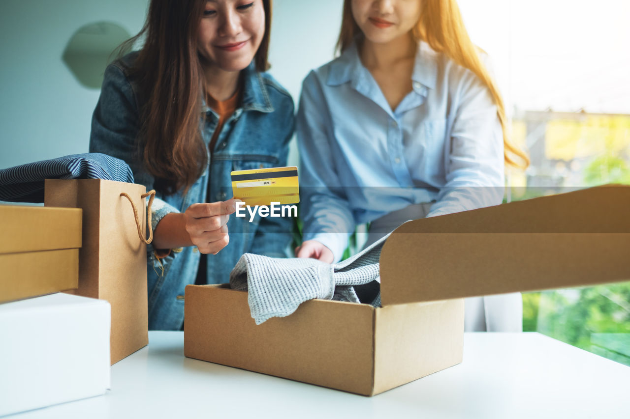 cardboard box, cardboard, box, women, adult, moving house, happiness, business, home ownership, smiling, two people, retail, female, container, young adult, indoors, holding, emotion, relocation, packing, cheerful, transportation, beginnings, paper, delivering, buying, shopping, lifestyles, casual clothing, communication, togetherness, finance, technology, architecture, customer, consumerism, friendship, looking, building, person, positive emotion