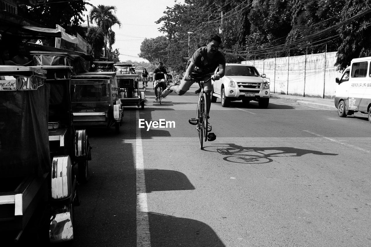 REAR VIEW OF MAN CYCLING ON ROAD