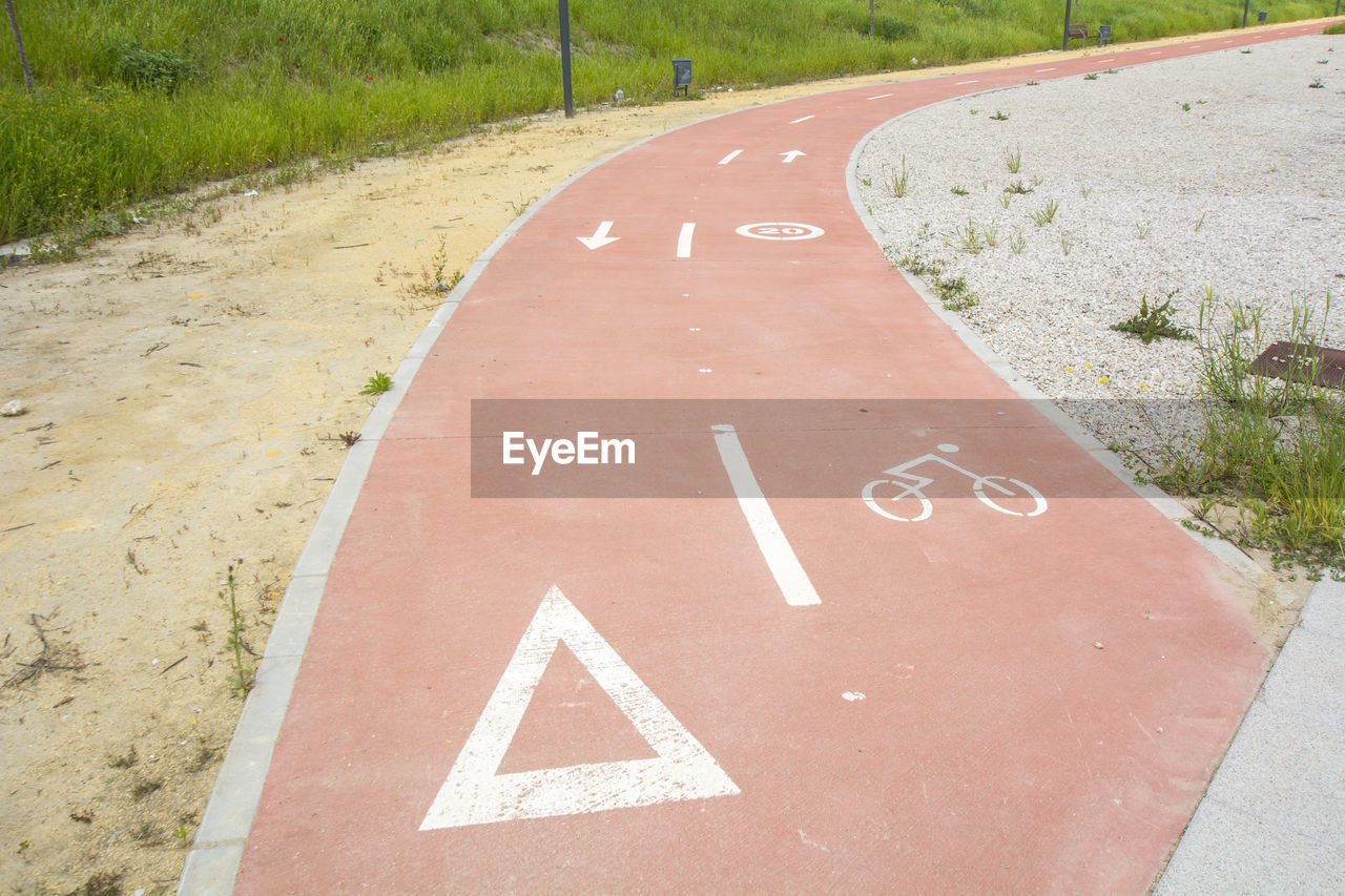 sign, road, lane, road surface, communication, asphalt, road sign, symbol, no people, guidance, infrastructure, sidewalk, the way forward, day, transportation, soil, arrow symbol, nature, number, text, road marking, outdoors, plant, marking, information sign, pedestrian crossing, walkway, high angle view, directional sign, bicycle lane, public space, tarmac