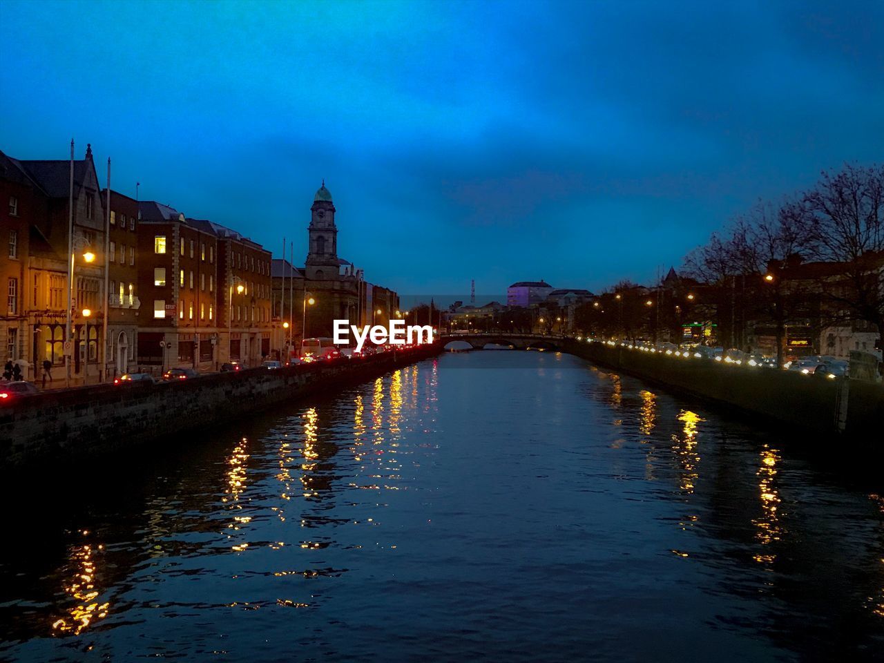 Illuminated buildings by river against sky at night