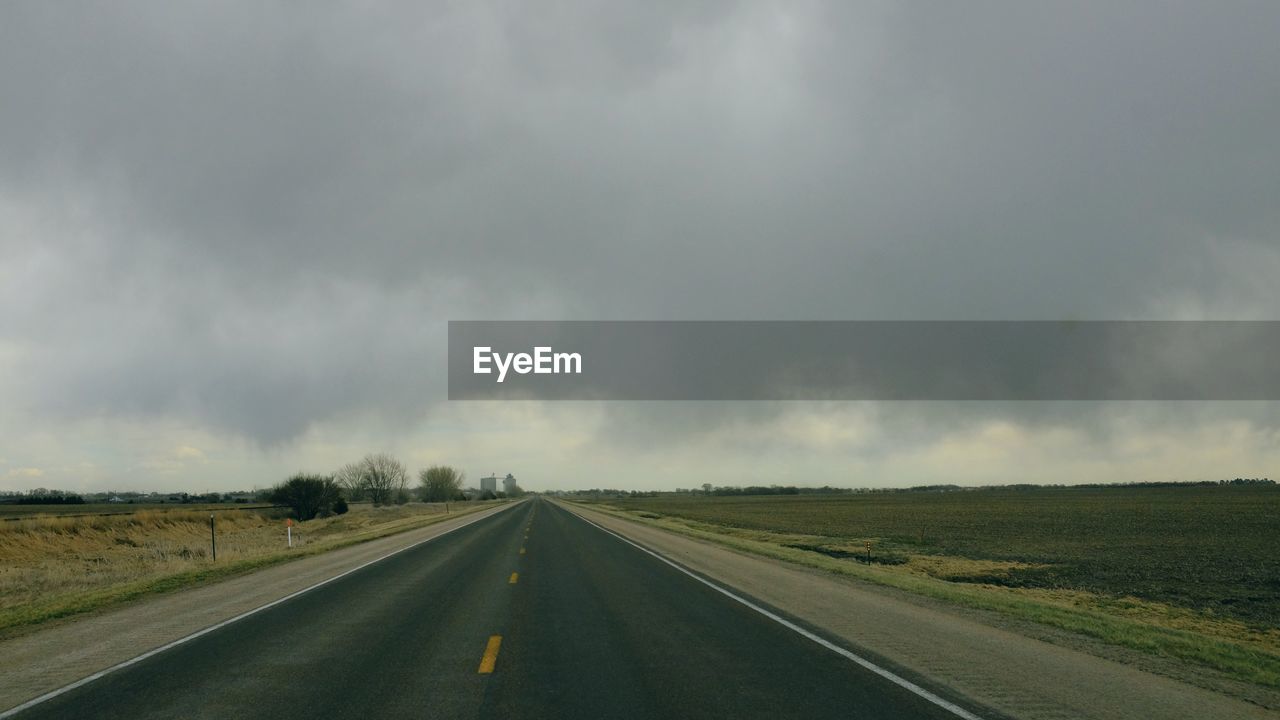 Road passing through landscape against storm clouds