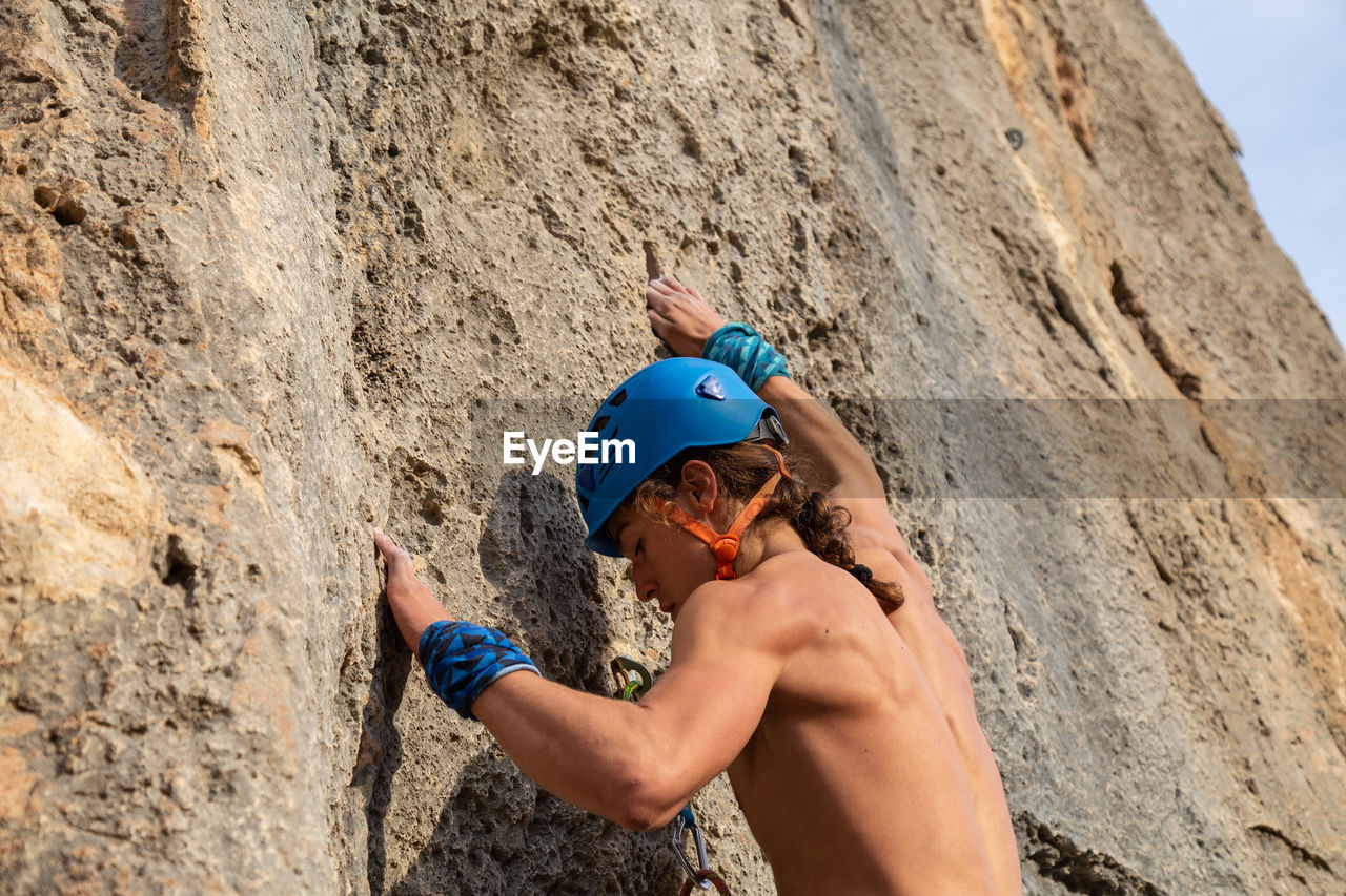 Shirtless man wearing helmet rock climbing