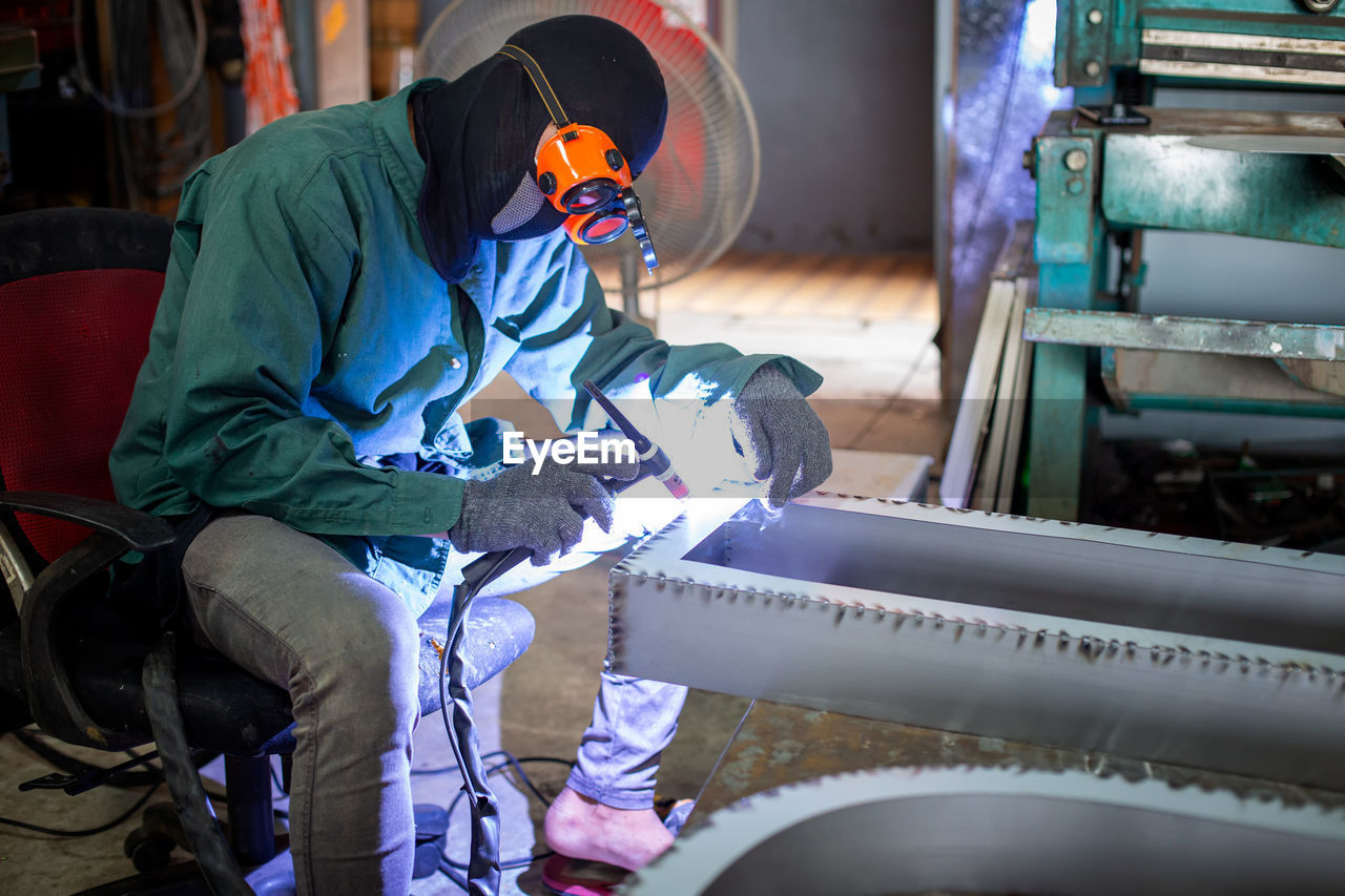The worker is welding steel frame in work shop.