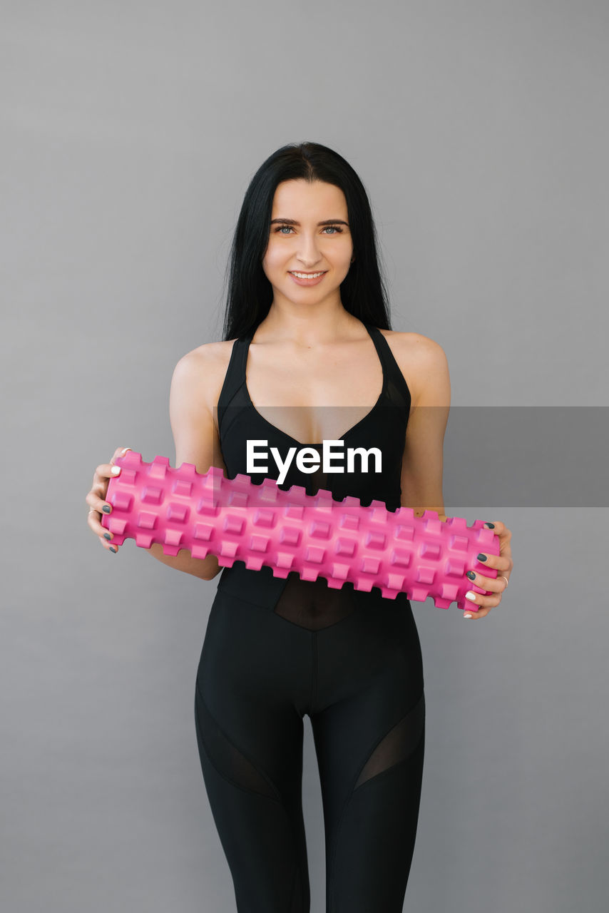 Fitness a woman in sports black clothes with a massage roller or a roll in her hands smiles