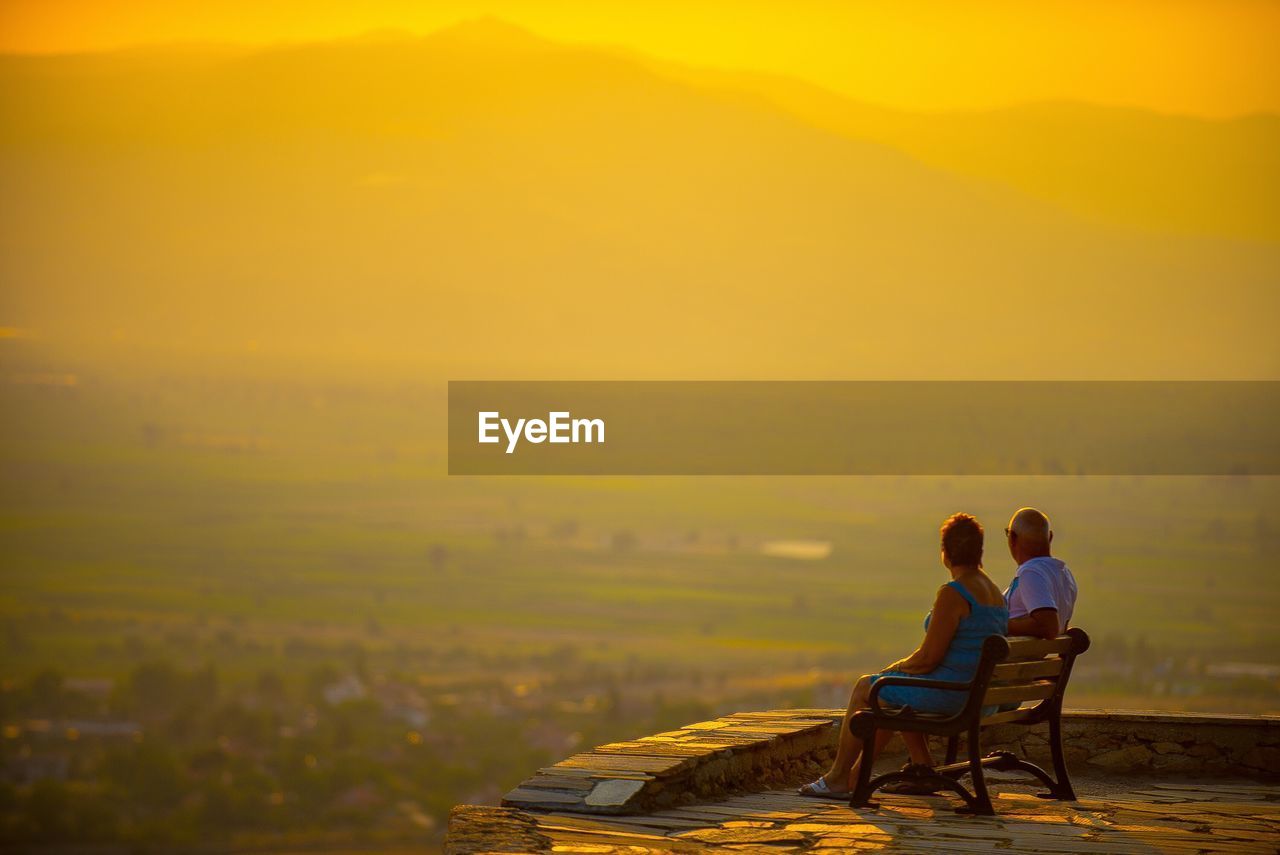 View of couple sitting on landscape against sky during sunset