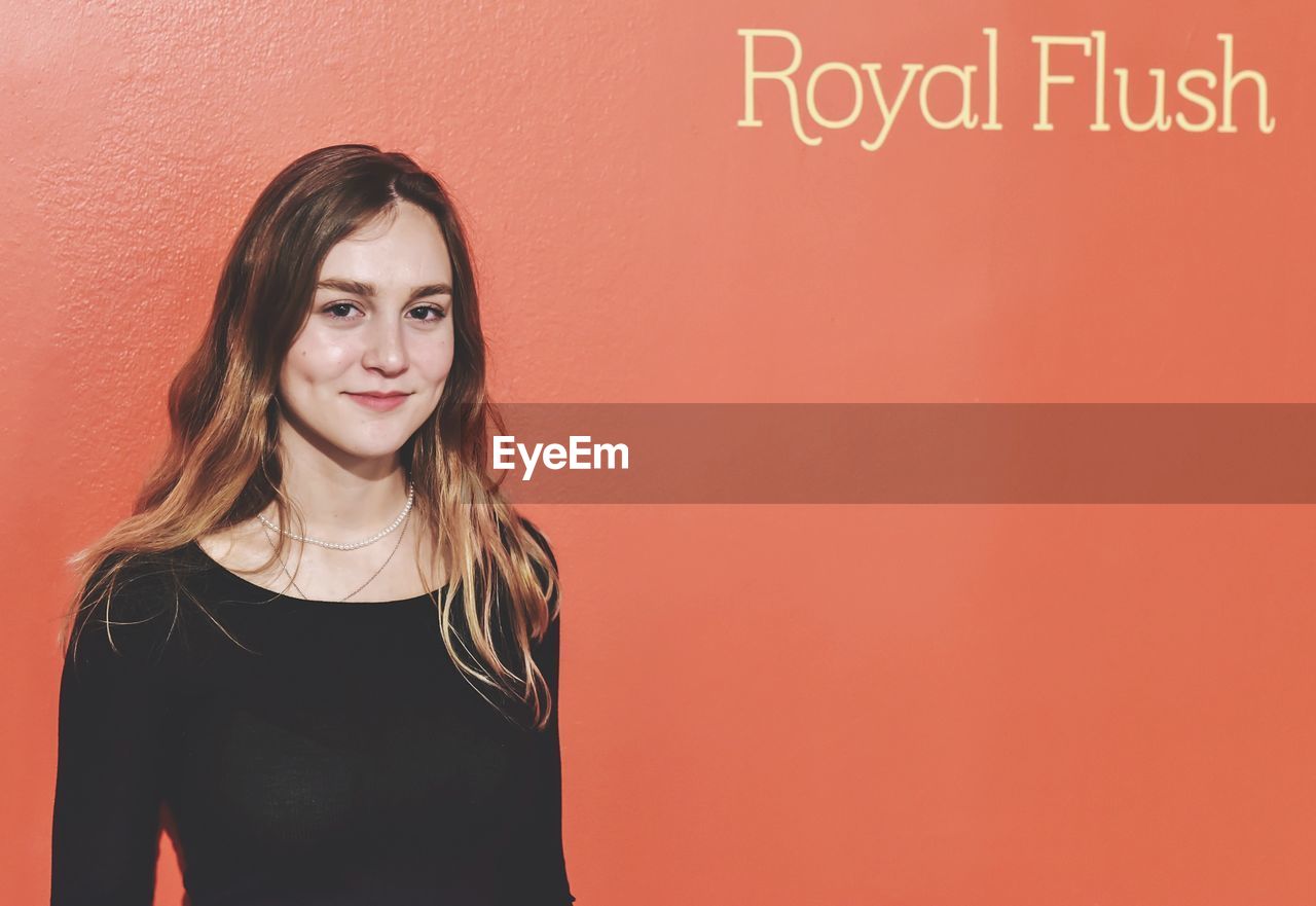 Portrait of smiling young woman standing against orange wall