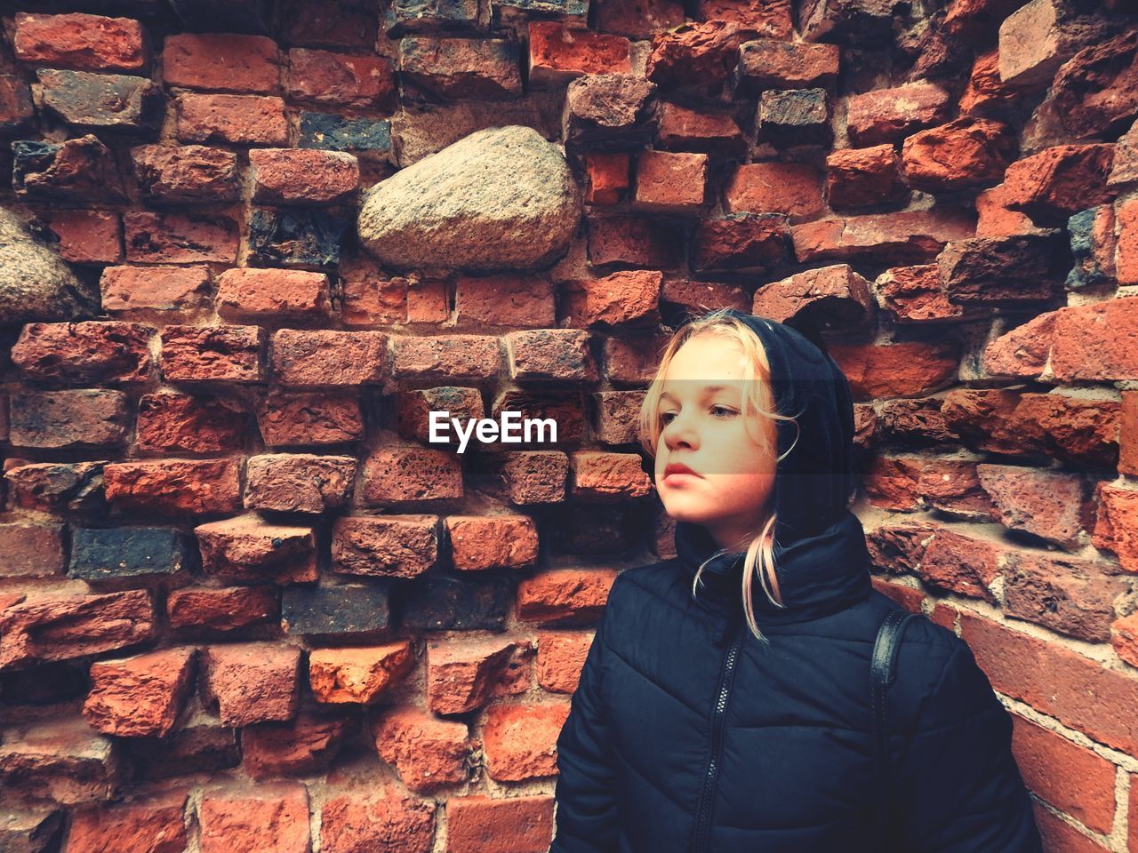 Girl looking away against brick wall