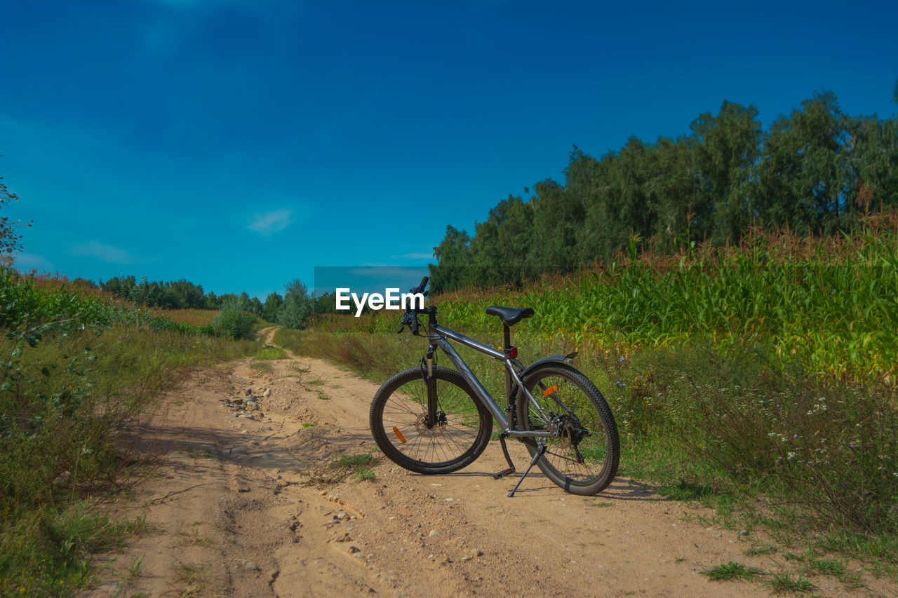 transportation, bicycle, soil, sky, mountain biking, plant, nature, mode of transportation, land, mountain bike, landscape, vehicle, cycle sport, environment, land vehicle, tree, travel, trail, scenics - nature, blue, road, cycling, sports equipment, beauty in nature, grass, activity, sports, no people, field, outdoors, dirt, non-urban scene, dirt road, tranquility, day, bicycle wheel, sunlight, footpath, rural scene, tranquil scene, adventure, mountain, green